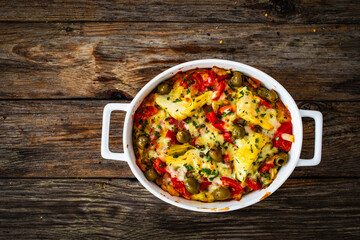 Bread casserole with mozzarella cheese, tomatoes, green olives, artichokes and scrambled eggs on wooden table
