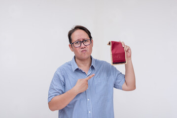 A middle aged asian man feeling down after pointing to an empty wallet devoid of cash. Bankrupt and...