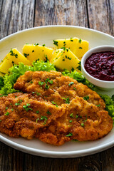 Crispy breaded seared chicken cutlet with boiled potatoes and beets on wooden table
