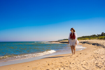 Fototapeta na wymiar Beautiful woman walking on sunny beach 