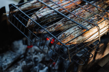 Fish omul on the grill. Four fish grilled on a grill on fire. Fresh seafood fish cooked over an open fire. Cooking barbecue fish on fire. - obrazy, fototapety, plakaty