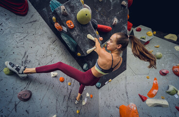 A strong female climber climbs an artificial wall with colorful grips and ropes.