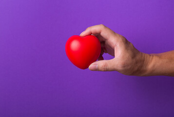Obraz premium Hand with red heart on purple background.