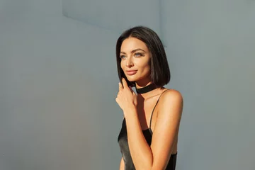 Fotobehang Kapsalon Female street sunny portrait of a beautiful young fashionable fresh woman model with a short brunette hairstyle with clear skin in a fashion black dress walking at sunset. Pretty lady outdoors  © alones