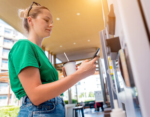 Young woman paying for coffee at vending machine using contactless method of payment 