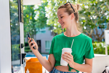 Young woman paying for coffee at vending machine using contactless method of payment 