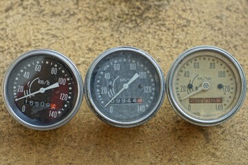 three glass round old ones for measuring speed with white arrows in an iron speedometer case from classic old java motorcycles lie on a yellow dirty table on the street