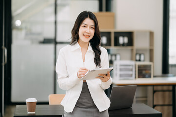 Confident business expert attractive smiling young asian woman holding digital tablet and laptop on desk in office...