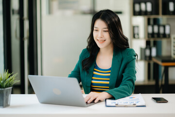 Beautiful Asian woman using laptop and tablet while sitting at her working place. Concentrated at work. in office..