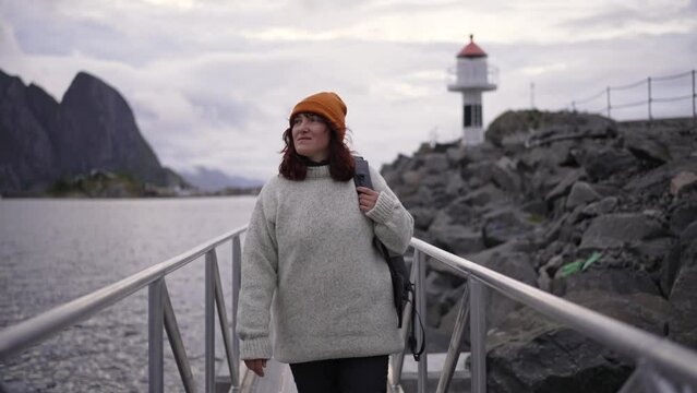 Against the backdrop of Reine, Lofoten, Norway, a young woman's journey to a white lighthouse is rendered in slow motion, imbuing the scene with a timeless quality.