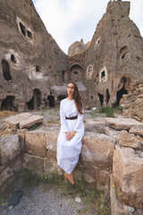 a beautiful girl in a long dress enjoys the view of the ancient architecture of the caves in Cappadocia