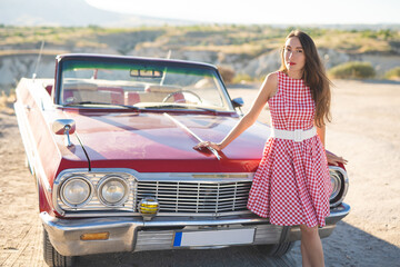beautiful girl in a retro dress at sunrise happy posing on the background of the mountain landscape in Cappadocia near a red retro car
