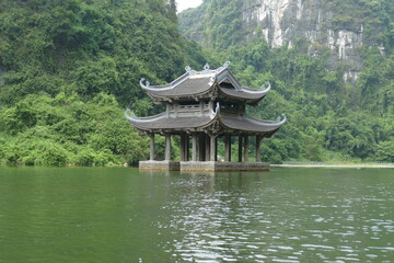 Templo orientas asiático sobre el agua con montañas y vegetación verde de fondo