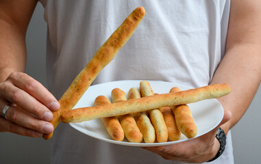 Mężczyzna trzymający w dłoniach talerz z drożdżowymi paluchami chlebowymi, przekąska imprezowa na słono 