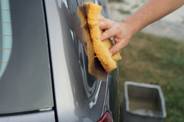 manual home washing by a washer with water using a yellow sponge and detergent to remove dirt from...