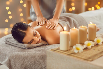 Obraz na płótnie Canvas Young woman relaxing in spa salon with hot stones along spine. Beautiful relaxed girl lying on couch enjoying hot stone massage in wellness center. Beauty treatment therapy, body care concept