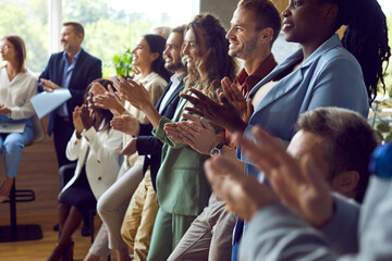 Group of happy joyful business people applaudding to speaker standing in a row in meeting room. Successful coworkers and company employees clapping a colleague on business training or conference.
