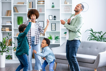 overjoyed family of four jumping to music in modern studio living room. Excited young married couple dancing with playful little children siblings, spending active free time at home.
