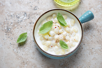 Turquoise serving bowl with italian chicche di patate in cheese sauce, horizontal shot on a beige stone background