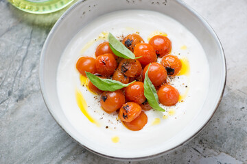 Bowl of tirokafteri or greek feta dipping sauce served with baked tomatoes, middle close-up on a...