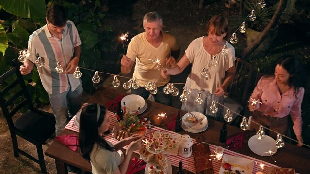 Top view. Family and friends gathering celebrating outdoor new year party and play festival sparklers together having enjoy at home. Big family multi-ethnic celebrating outdoors party at garden.