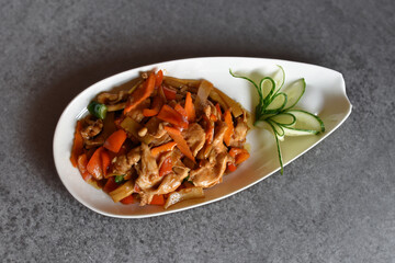 Spicy meat mixture with vegetables. Asian food prepared in a wok pan. Chopped carrot and green pepper. Cucumber garnish