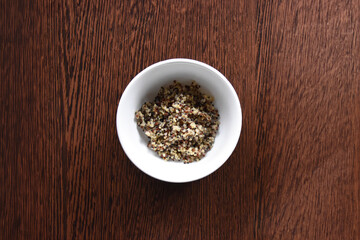 White porcelain bowl with freshly cooked quinoa. On a wooden table. To prepare the salad. Top view
