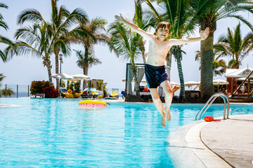 Happy little kid boy jumping in the pool and having fun on family vacations in a hotel resort. Healthy child playing in water.