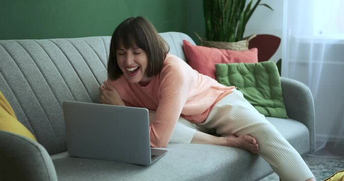 In the welcoming living room, a woman sits on the couch, her laughter filling the space as she works on her laptop. Her infectious mirth adds an element of joy and positivity to the room.