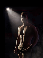 A shirtless muscular man standing in front of a spotlight. Photo of a shirtless man standing in front of a spotlight
