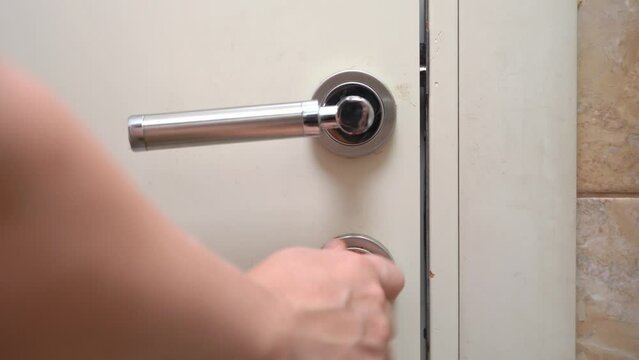 Person hand pressing metal door handle tightly closes door in bathroom. Woman wants to spend time in privacy in bathroom at home