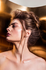 Beauty portrait of model with natural make-up and hair styling on the gold background. Fashion shiny highlighter on skin and gloss lips 