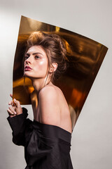 Beauty portrait of model with natural make-up and hair styling on the gold background. Dressed in black