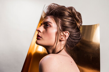 Portrait of female fashion model with naked shoulders and long hair looking up over gold background. Beautiful woman with trendy make-up