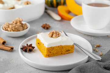 Spiced pumpkin cake with walnut and cream cheese frosting sliced into squares on a gray concrete background. Autumn dessert.