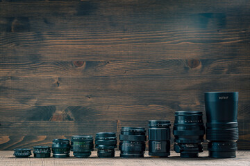 Set of vintage camera lenses from the times of the USSR on a wooden background, closeup, copy space. Line of old retro lenses from small to large