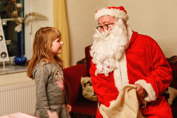 Little toddler girl talking to Santa Claus called Nikolaus or Weihnachtsmann in German. Happy smiling kid waiting for gifts. Santa with golden book. Xmas, childhood, holiday