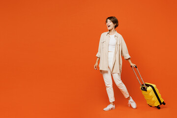 Side view happy traveler woman wears casual clothes hold bag suitcase isolated on plain orange red background. Tourist travel abroad in free spare time rest getaway. Air flight trip journey concept.