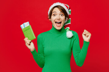 Traveler woman wears green casual clothes Santa hat hold passport ticket do winner gesture isolated...