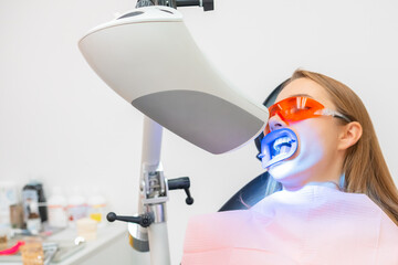 A female patient receives teeth whitening treatment, including the use of a UV lamp for bleaching...