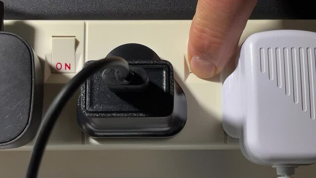 Closeup of a man's hand inserting an electrical plug into a spare socket on an extension board, then switching the power on.
