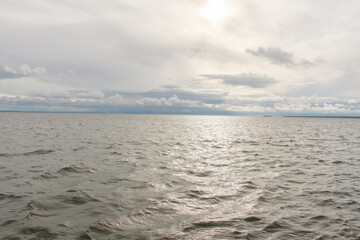 Seascape: waves on the sea on a cloudy day, with the sun breaking through the clouds, shining its rays onto the water