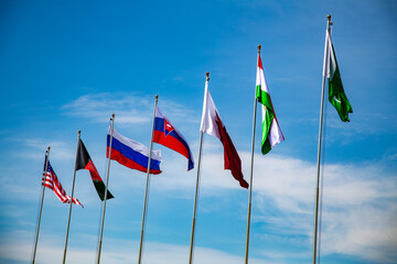 multiple different flags from different countries with a blue sky dancing to the wind