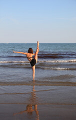 Fototapeta na wymiar girl with black swimsuit performing gymnastic exercises on the beach
