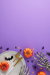 Obraz premium Nurturing the perfect Halloween atmosphere at your dining table. Top view vertical shot of plates, cutlery, scary skeleton arms, pumpkins, spooky elements on violet background with ad space
