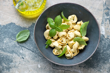 Bowl with raw tortelloni, fresh green basil and olive oil on a grey and beige stone background, horizontal shot, high angle view