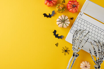 Picking out Halloween presents with a few clicks. Top view shot of laptop, skeleton hands, pumpkins, scary elements on yellow background with marketing space - obrazy, fototapety, plakaty