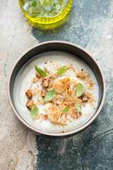Bowl of cauliflower cream-soup on a grey and beige granite background, vertical shot, elevated view