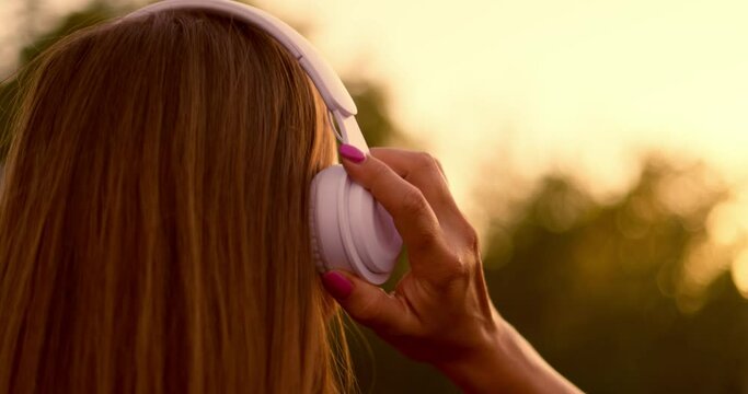 Woman puts on headphones, listens to music and dances at sunset.