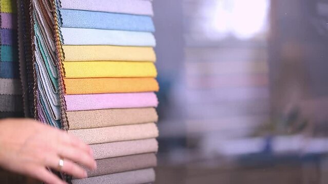 Fabric swatches in different colors are stacked for selection. The client chooses the shade of fabric for decorating. A variety of shades of upholstery material for furniture and interior.